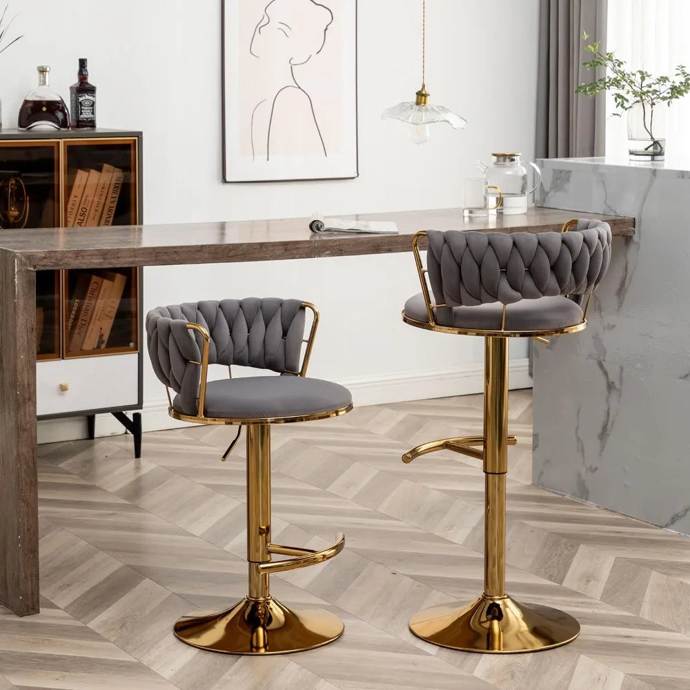 The Morsale Counter Height Velvet Bar Stools Set of 4, featuring gold frames and tufted grey seats, are arranged at a sleek wooden bar counter. A minimalist line art portrait decorates the wall, while a pendant light illuminates the marble-topped counter in this bright, modern space.