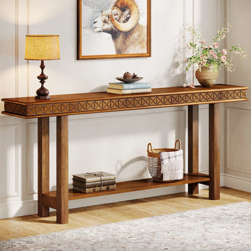 The Stanton Entryway Table With Storage by Morsale stands against a geometric-patterned wall, adorned with a lamp, books, and a vase of flowers. Below, a woven basket and more books sit on the lower shelf. A framed ram picture hangs above in this stylish piece of living room furniture with light walls and wooden flooring.