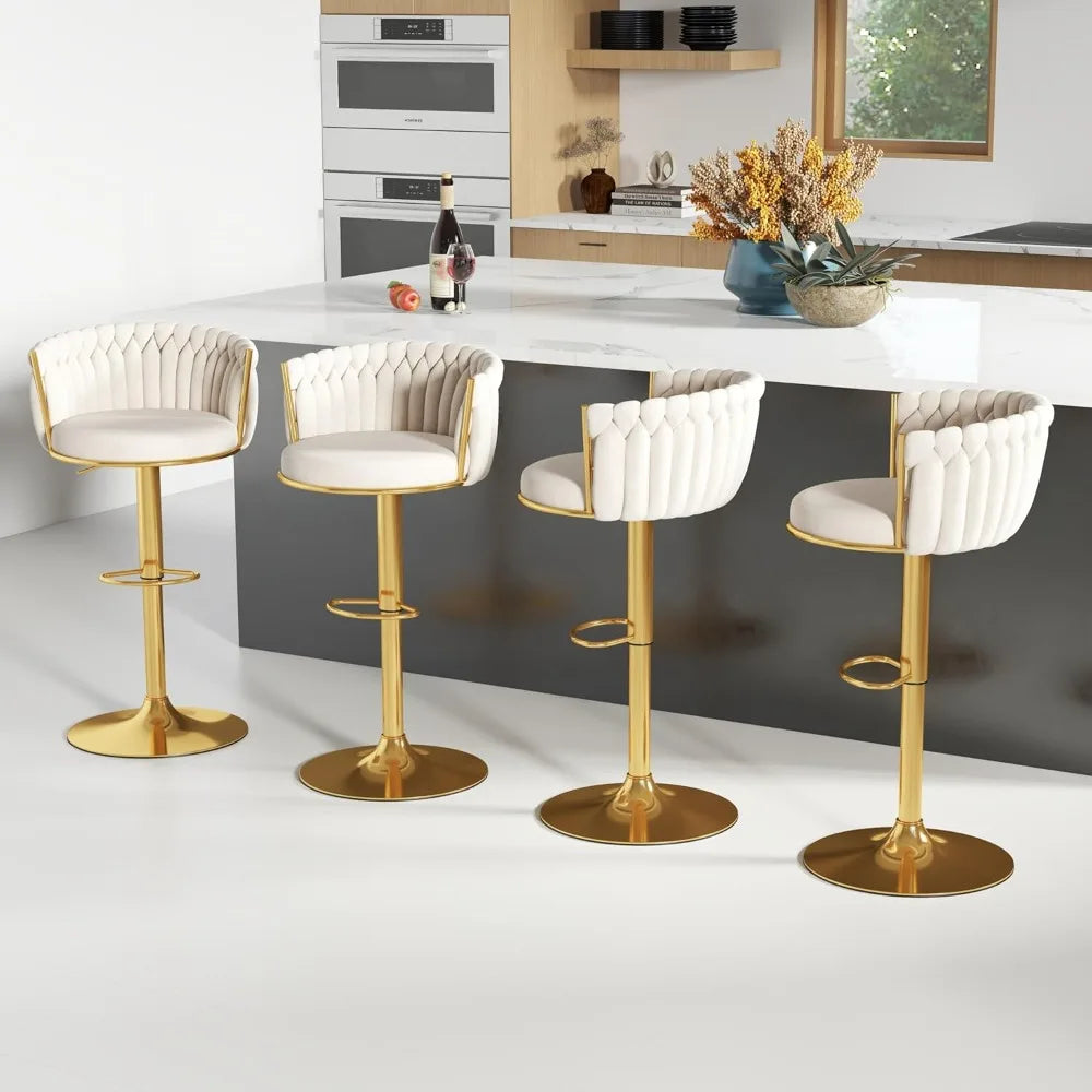 A modern kitchen features a sleek white island with four Morsale height adjustable counter stools, boasting tufted upholstery in gold. Wooden cabinets, a built-in oven, a plant arrangement, and a window backdrop complete the scene. A bottle and glasses sit invitingly on the counter.