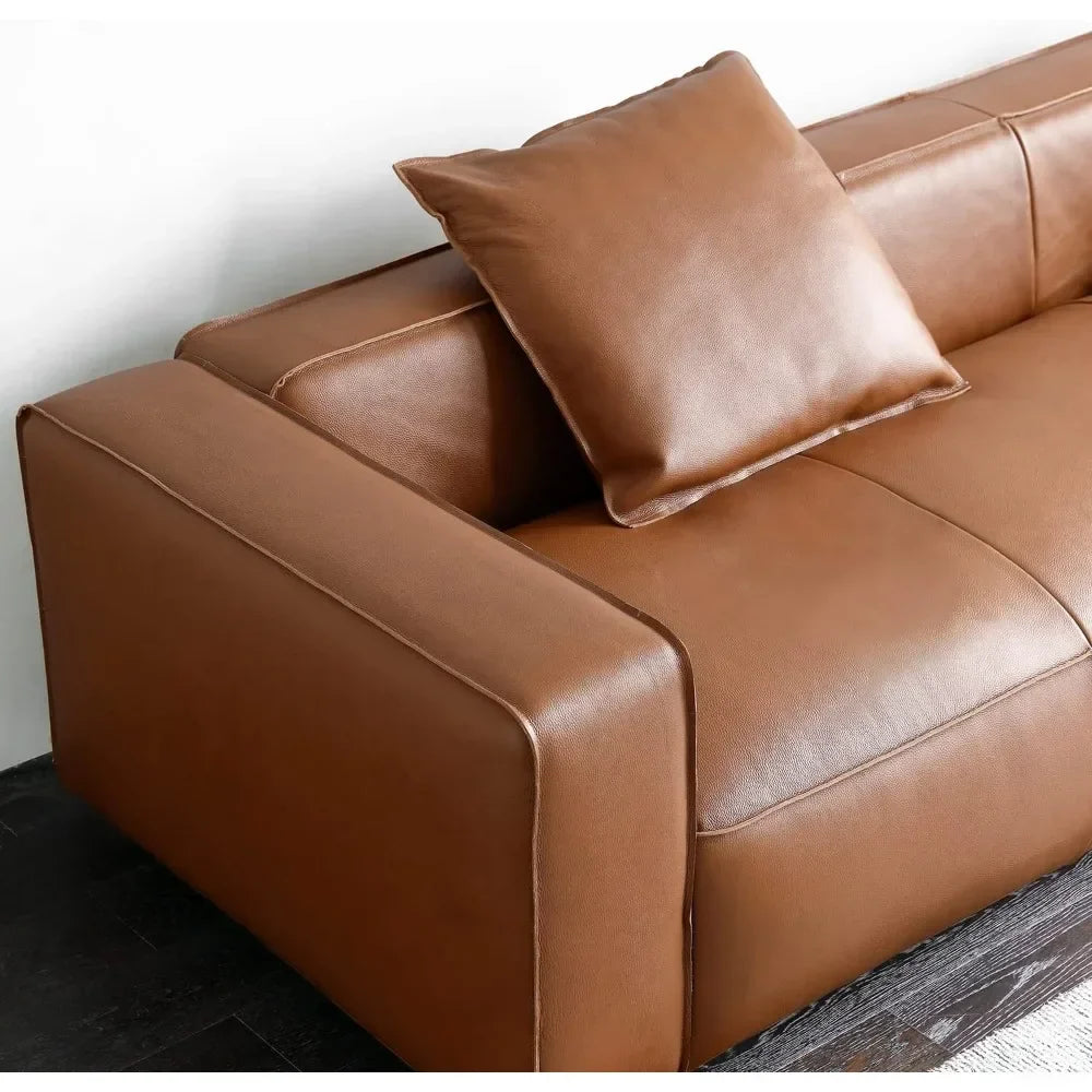 The Morsale Stefano Genuine Leather Lounge Sofa is a modern brown leather piece featuring minimalist lines, complemented by a matching cushion on one side. It’s elegantly positioned against a white wall on a dark wood floor.