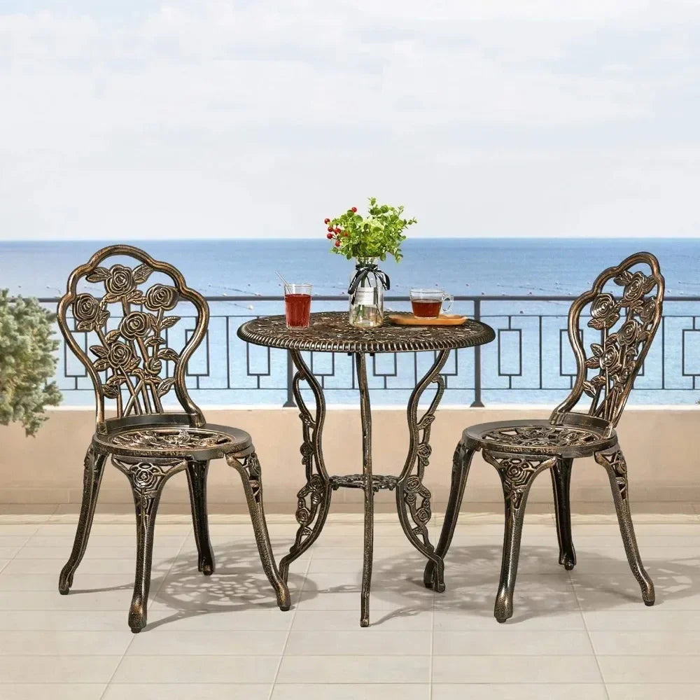 On the patio, the Davids 3-Piece Vintage Outdoor Set by Morsale features two ornate metal chairs and a round table with drinks and a plant. The area is bordered by a decorative railing, enhancing the tranquil seaside ambiance. The background showcases Morsale's stunning ocean view under a clear sky.
