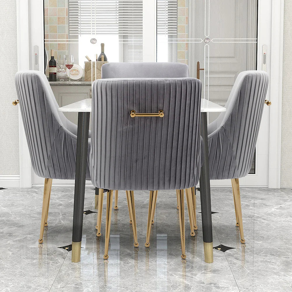 The modern glam dining area highlights a white table with the Morsale Modern Glam Boucle Pleated Velvet Dining Chair Set of 4, featuring gold legs, a vertical ribbed design, and gold handles. A bottle of wine and glasses enhance the elegance against gray marble flooring.