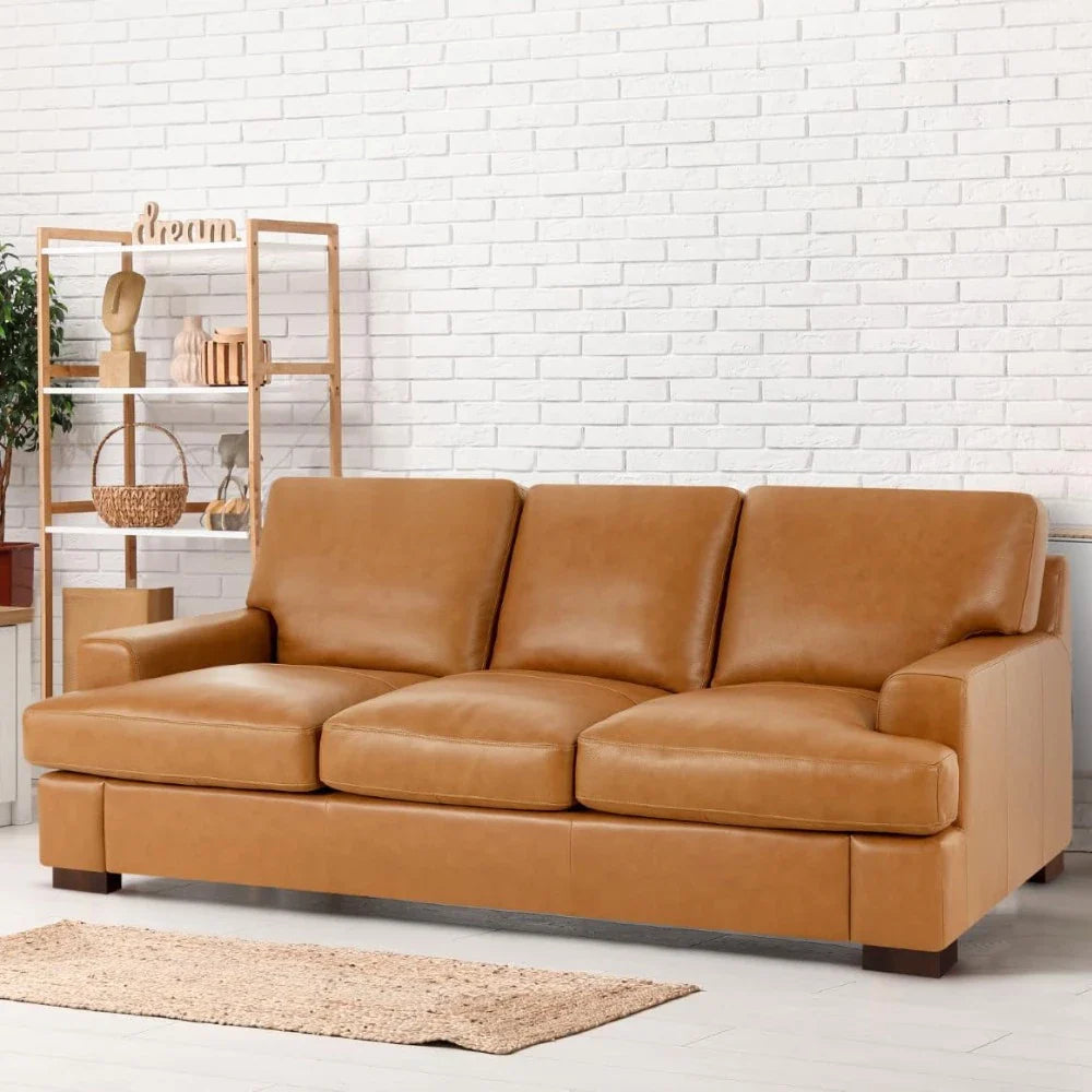 The Morsale Piazze Genuine Leather Sofa with three cushions sits against a white brick wall, anchoring the modern style. To the left, a wooden shelf displays plants and pottery, while a woven rug completes this inviting living room setup.