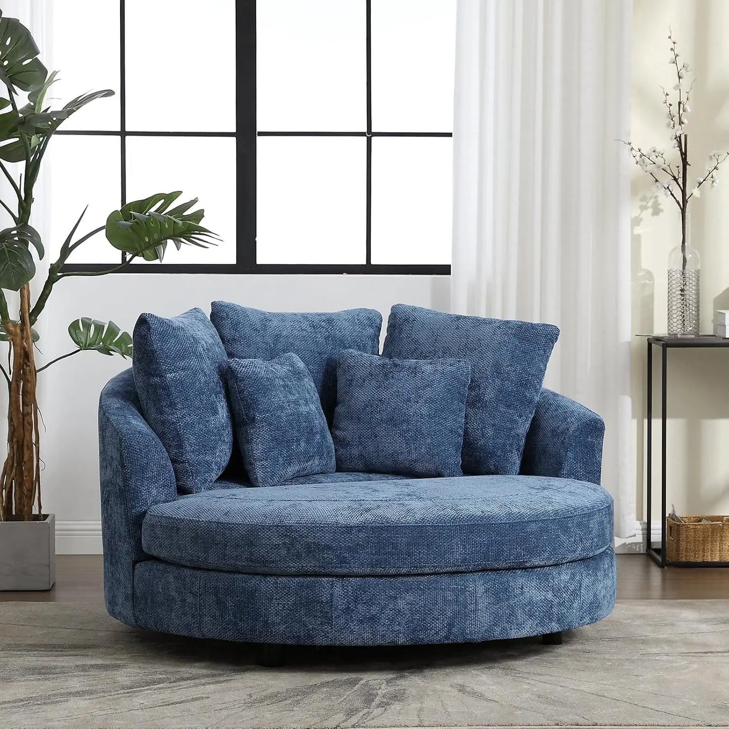 The Morsale 59.8" Oversized Accent Barrel Sofa Chair, featuring a solid wood frame and textured upholstery, is styled with five matching cushions. It adds charm to a sunlit room adorned with potted plants, bright windows, white curtains, and a sleek console table.