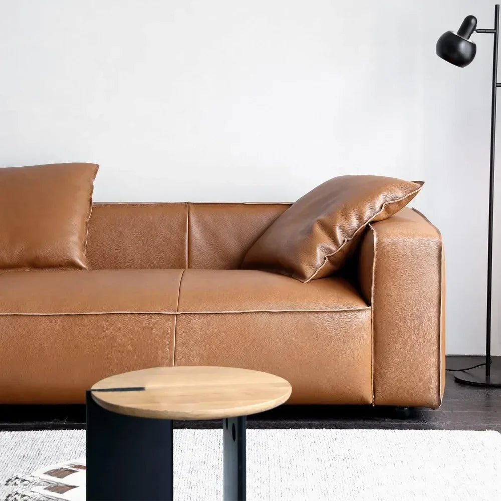 A contemporary living room features the Morsale Stefano Genuine Leather Lounge Sofa in chic brown, adorned with two pillows. A round wooden coffee table complements it, while a black floor lamp stands elegantly against a white wall.