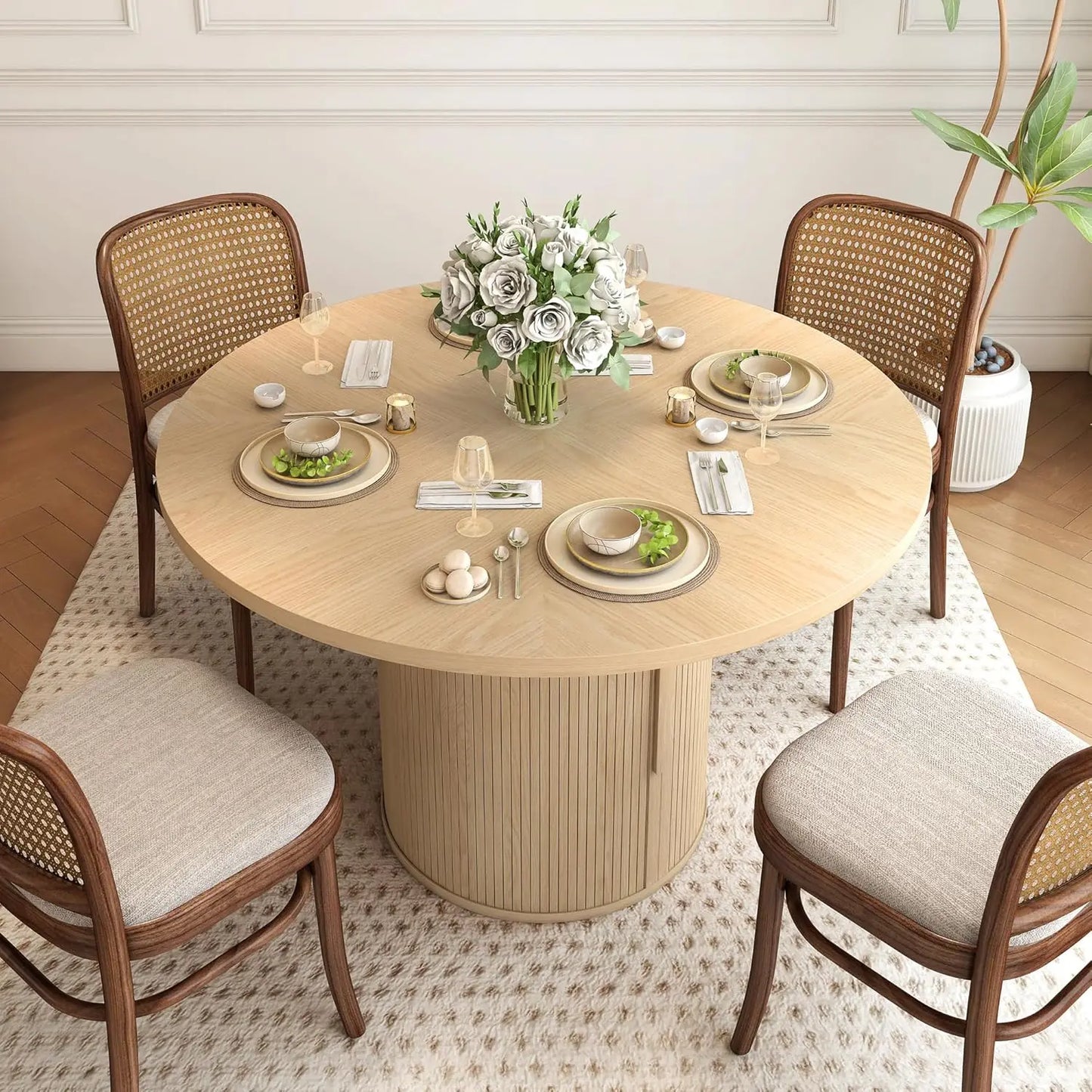 The Morsale Harrow 47" Round Dining Table With Storage sets a modern scene, with white plates, cutlery, glasses, and bowls of greens. A floral centerpiece featuring white flowers adorns the middle. Four cushioned chairs rest on a textured rug, complemented by a plant in the corner.