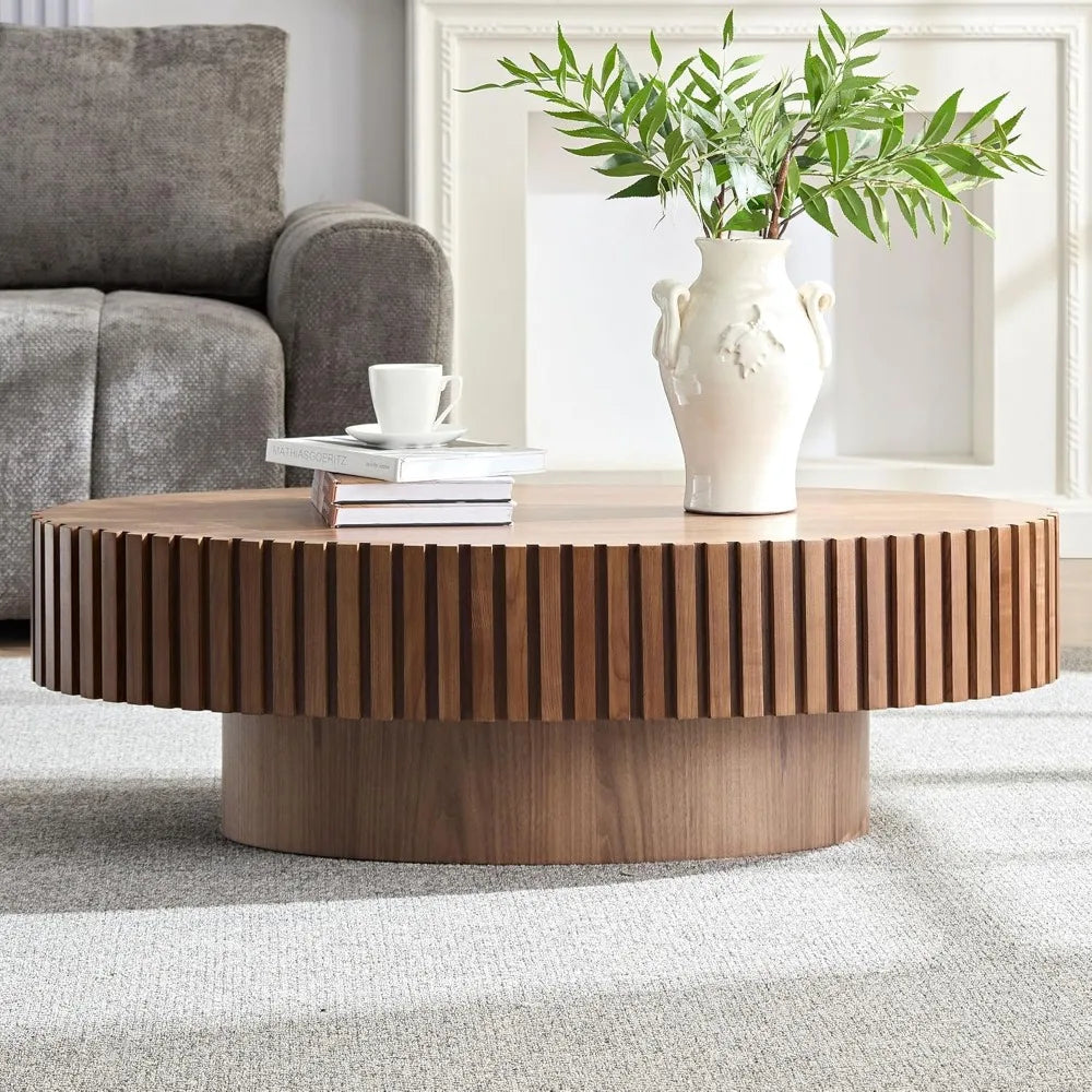 A 43" Morsale wooden coffee table with a textured design holds a white vase with green foliage. Two books and a white cup sit beside the vase, framed by a gray couch and white fireplace in the background for an elegant touch.