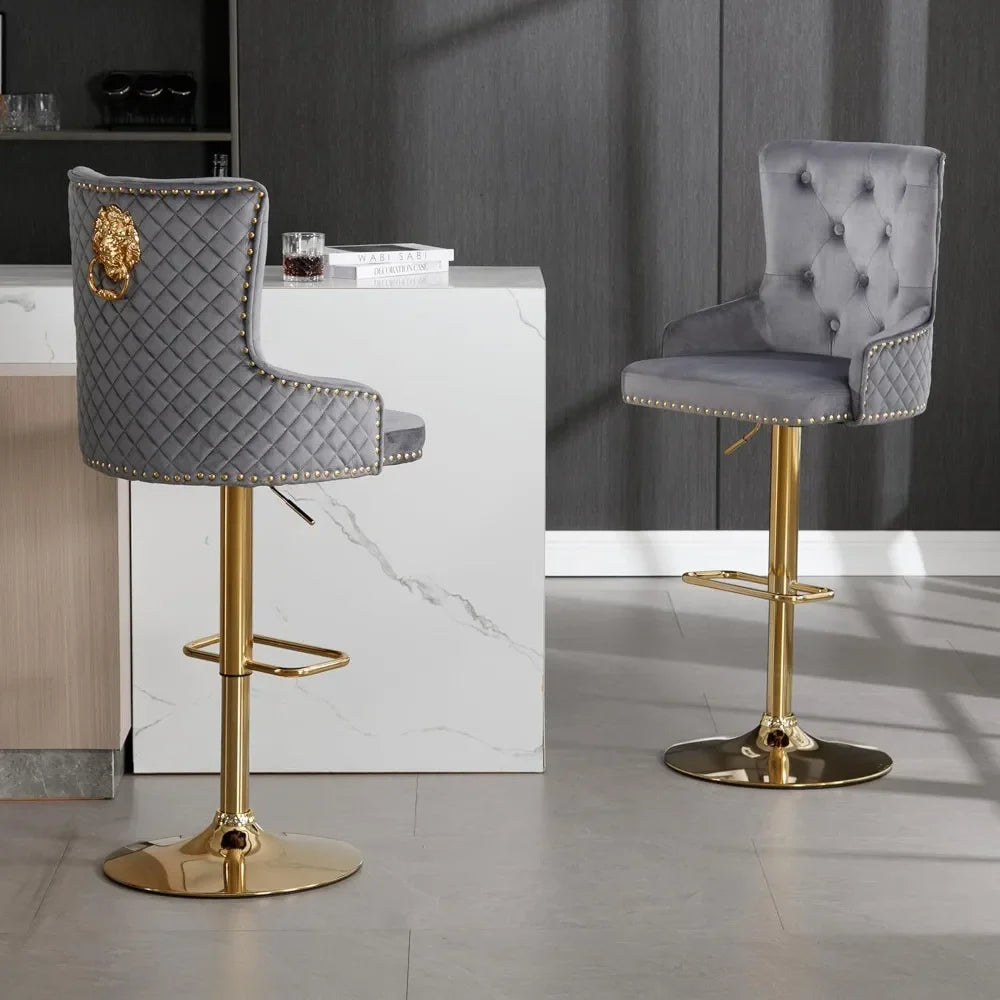Morsale's Diamond Lattice Wingback Counter Stools elegantly accompany a marble-topped counter with quilted gray upholstery and gold bases. One stool has a lion emblem, enhancing the minimalist room's modern charm, featuring dark walls and a light floor.