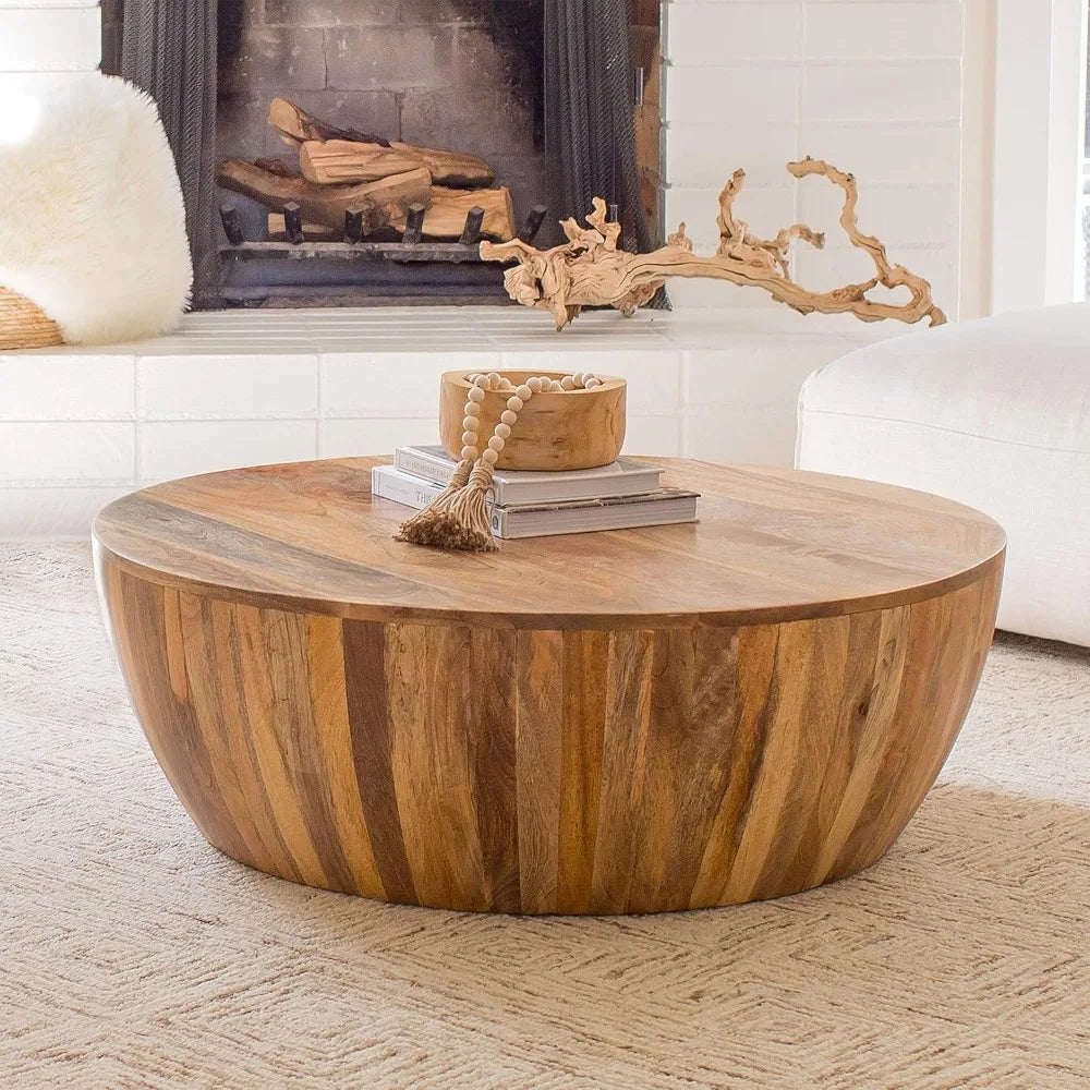 The Morsale Mango Wood Goa Coffee Table sits on a beige carpet in front of a modern fireplace with stacked logs. It's adorned with a wooden bowl, book, and decorative bead string. Part of a white sofa is nearby.