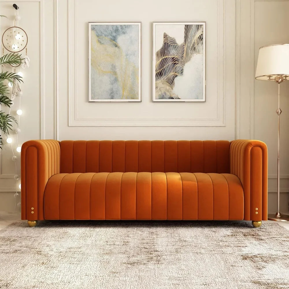 An 80" Morsale Velvet Living Room Sofa in luxurious orange with vertical tufting enhances the chic living room. Above, two abstract paintings add flair. A round clock, string lights to the left, and a tall floor lamp on a textured rug complete this elegant furniture setup.