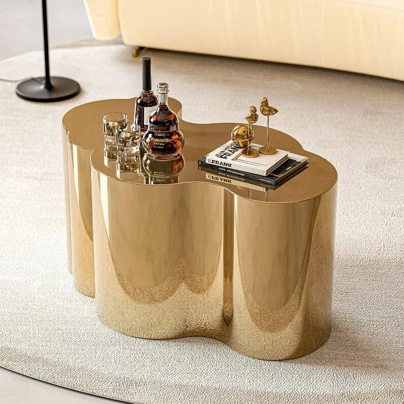 The Morsale Stainless Steel Gold Coffee Table sits on a light rug, adorned with a bottle, two glasses, books, and a small decorative piece. A beige sofa and sleek black floor lamp can be seen partially in the background.