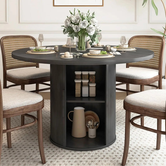 The Harrow 47" Round Dining Table With Storage by Morsale exudes a modern farmhouse charm, pairing with four chairs featuring elegant beige cushions. The dark table hosts storage shelves, adorned with a vase of white roses, complemented by soft rugs and light-colored walls for a tasteful setting.
