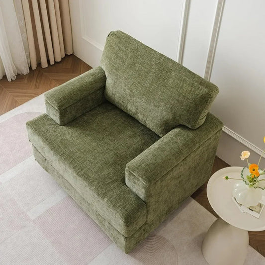 A cozy living room showcases a Morsale Oxford Lounge Chair With Armrests in plush green, resting on a light-patterned rug. Beside it stands a small round white table holding yellow flowers. The floor has a wooden herringbone design, complemented by curtains against the wall.