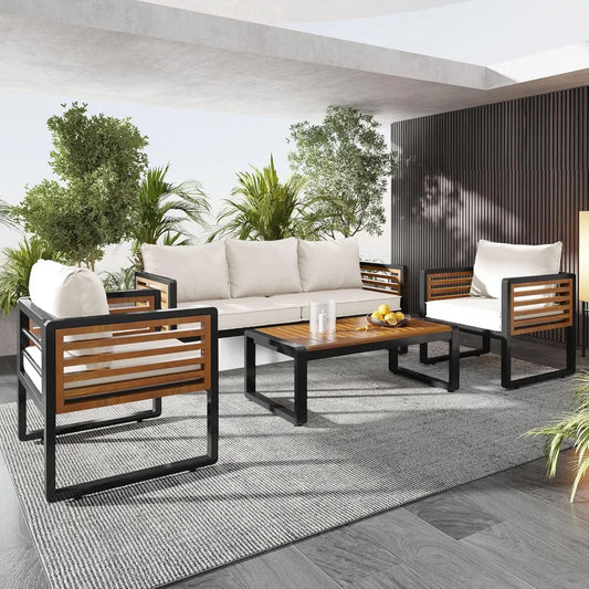 The Morsale 4-Piece Outdoor Patio Sectional Sofa Set includes an Acacia Wood table, sectional sofa, and two chairs with white polyester cushions. Complemented by lush green plants, a gray rug, and a slatted wall backdrop, it creates a cozy and stylish modern design.