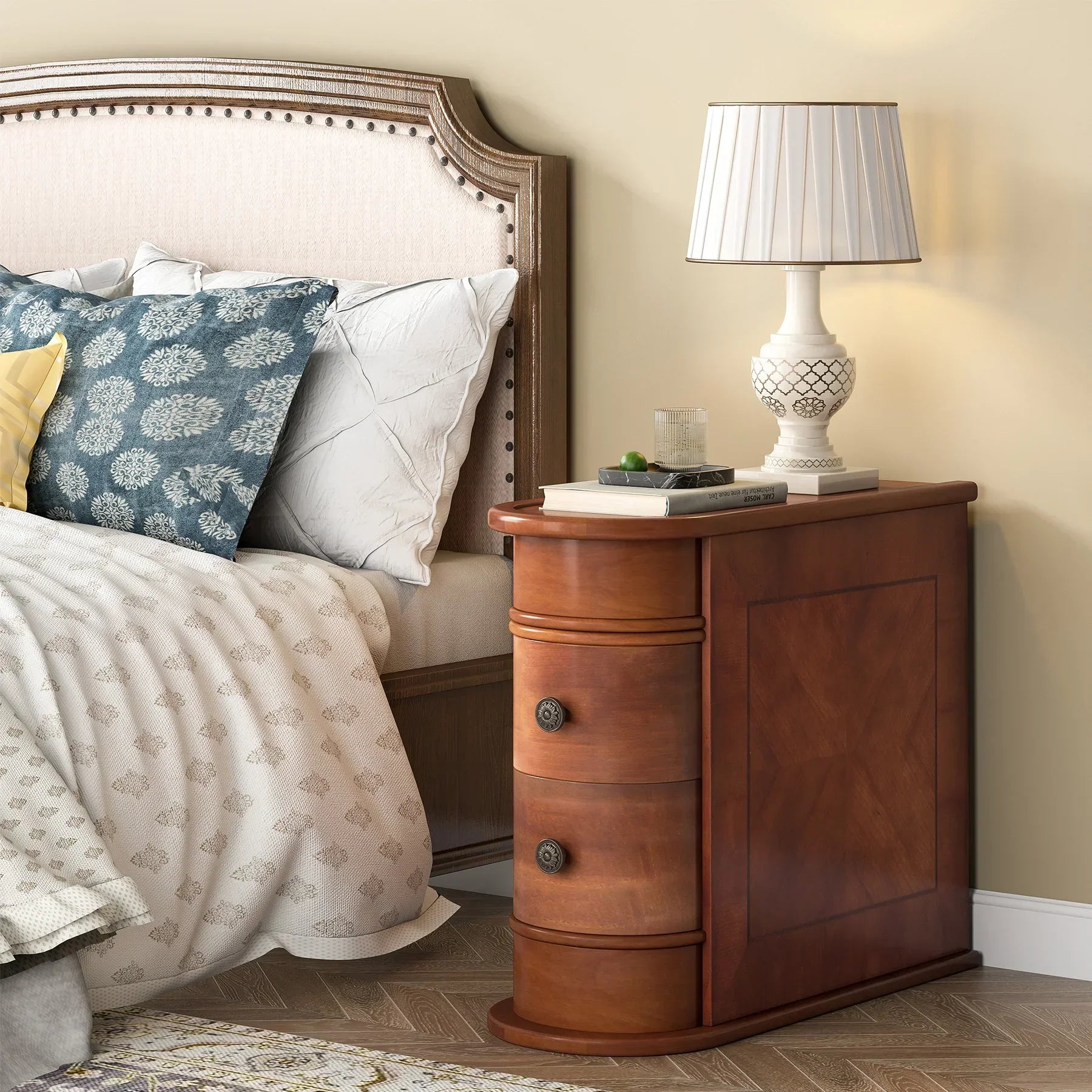 Beside the bed, adorned with patterned pillows and a duvet, sits the Morsale Irvine Solid Wood Side Table. Atop it are a lamp with a pleated shade and a book. The bed features an upholstered headboard with tufted details, enhancing the room's modern style.