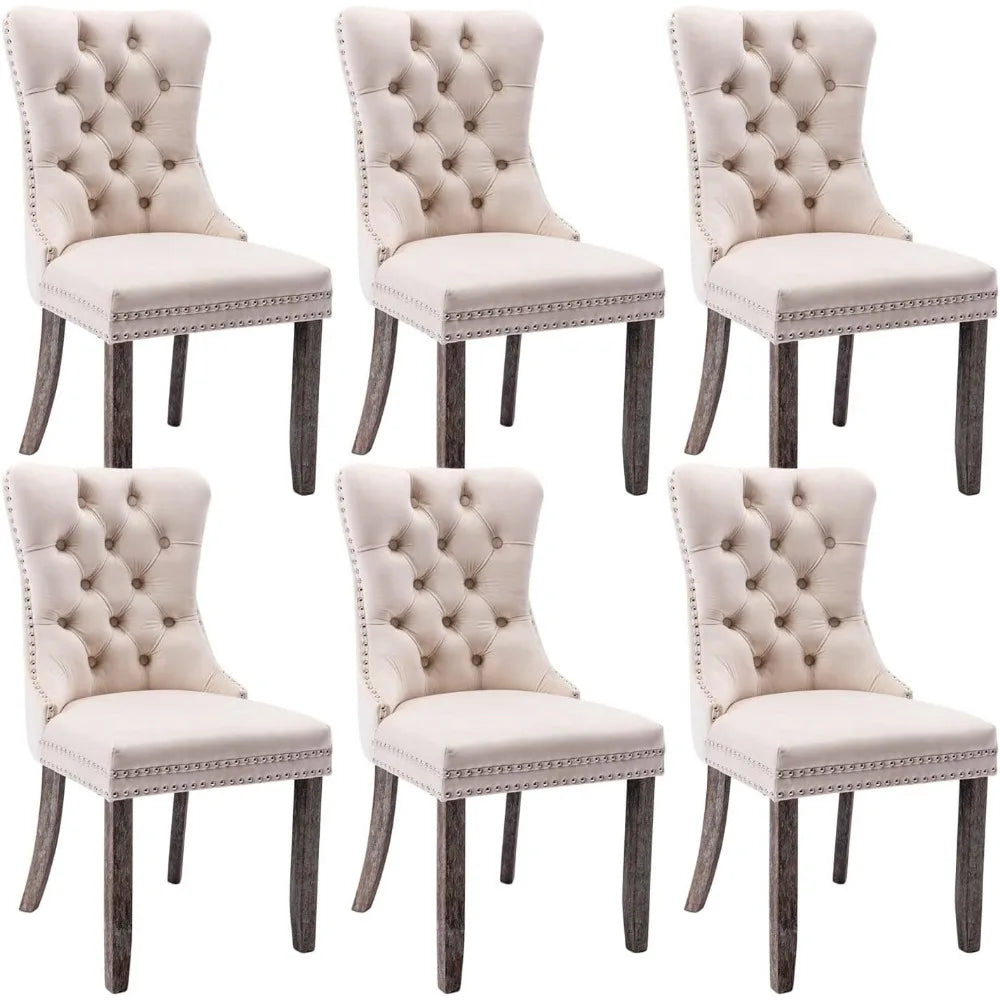 A set of Morsale Velvet Tufted Dining Chairs in beige with nailhead trim complements the wooden table, exuding a minimalist modern vibe. A sleek vase with white flowers sits on a brown shaggy rug, while framed art and a bright window enhance the serene atmosphere.