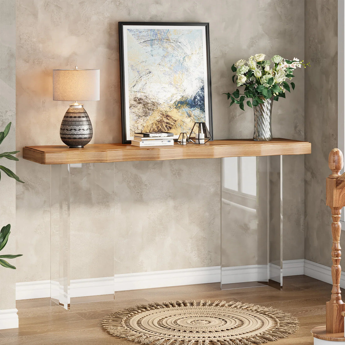 In a modern hallway, the Martin 47" Entryway Table with clear acrylic legs by Morsale displays books, a black vase with red berries, and a patterned lamp. A round mirror decorates the textured gray wall above. Nearby, a woven basket complements this chemical-free décor inspired by Mainland China craftsmanship.