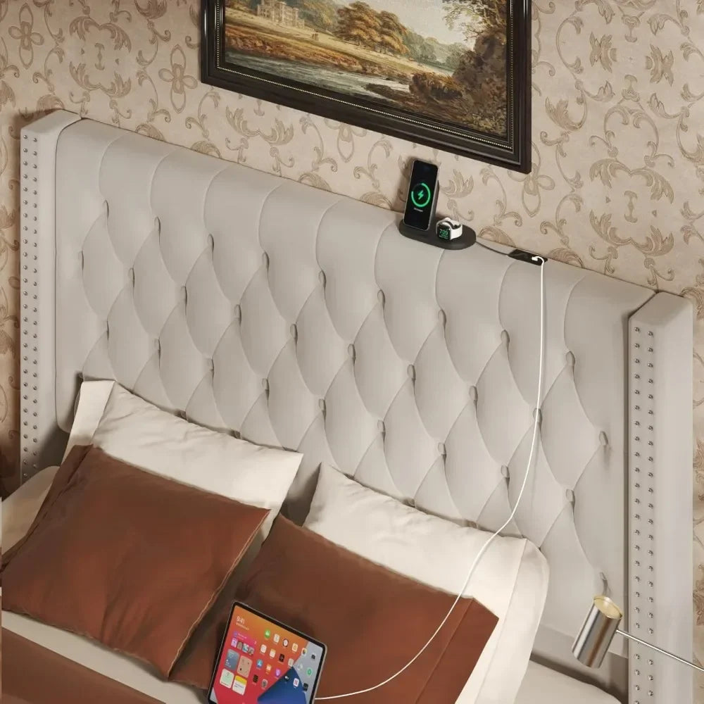 The Gio Velvet Queen Bed with Storage by Morsale showcases modern style with its tufted, light-colored headboard. It's adorned with brown and white cotton pillows, set against a patterned wall. A smartphone charges on the headboard, a tablet rests on the bed, and an elegant painting hangs above.