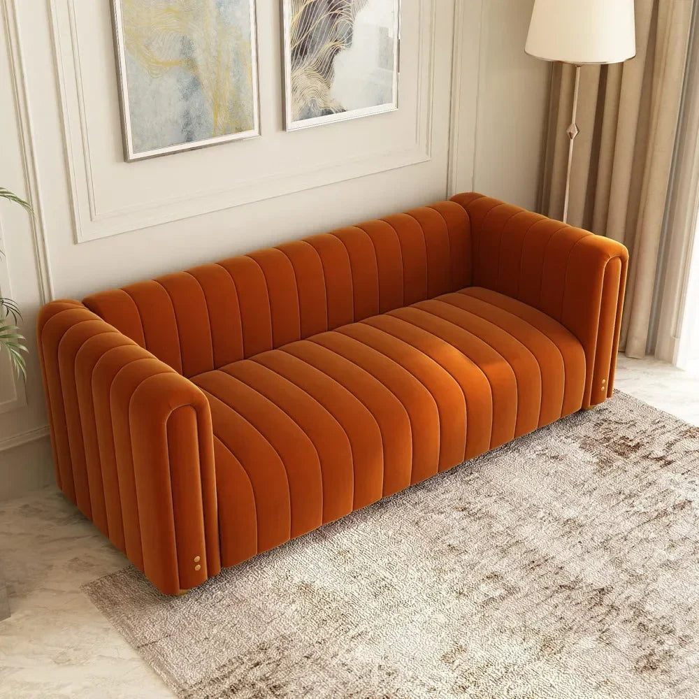 A Morsale 80" velvet living room sofa in orange velvet rests on a patterned rug in the cozy living room. Light walls feature abstract art, and a floor lamp by the curtained window enhances the charming furniture setup.
