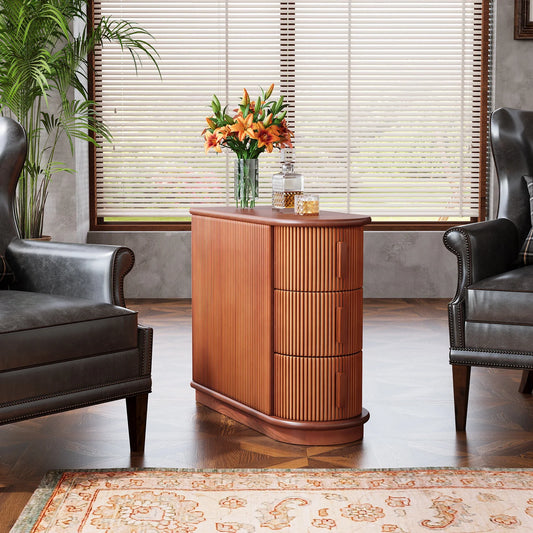 A stylish living room showcases two dark leather armchairs flanking the Morsale Irvine Solid Wood Side Table, featuring vertical grooves. A vase of orange lilies and decorative jars adorn the table. Natural light streams through large windows with horizontal blinds, highlighting a patterned rug.