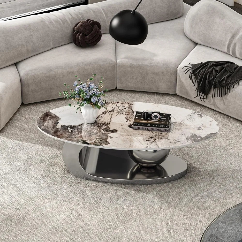 A modern living room features a curved beige sofa embracing a Morsale Modern Coffee Table with a steel base and ceramic top. This elegant space, adorned with a Chemical Free floral arrangement and book, is lit by a black pendant light, while a gray throw blanket adds coziness to the sofa.