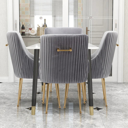 The modern glam dining area highlights a white table with the Morsale Modern Glam Boucle Pleated Velvet Dining Chair Set of 4, featuring gold legs, a vertical ribbed design, and gold handles. A bottle of wine and glasses enhance the elegance against gray marble flooring.