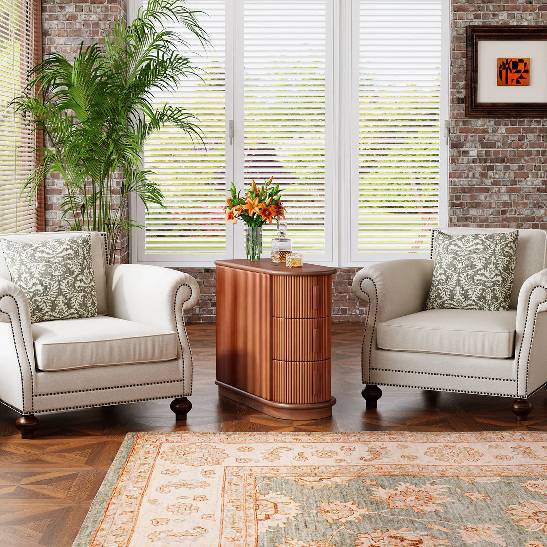 A stylish living room showcases two dark leather armchairs flanking the Morsale Irvine Solid Wood Side Table, featuring vertical grooves. A vase of orange lilies and decorative jars adorn the table. Natural light streams through large windows with horizontal blinds, highlighting a patterned rug.