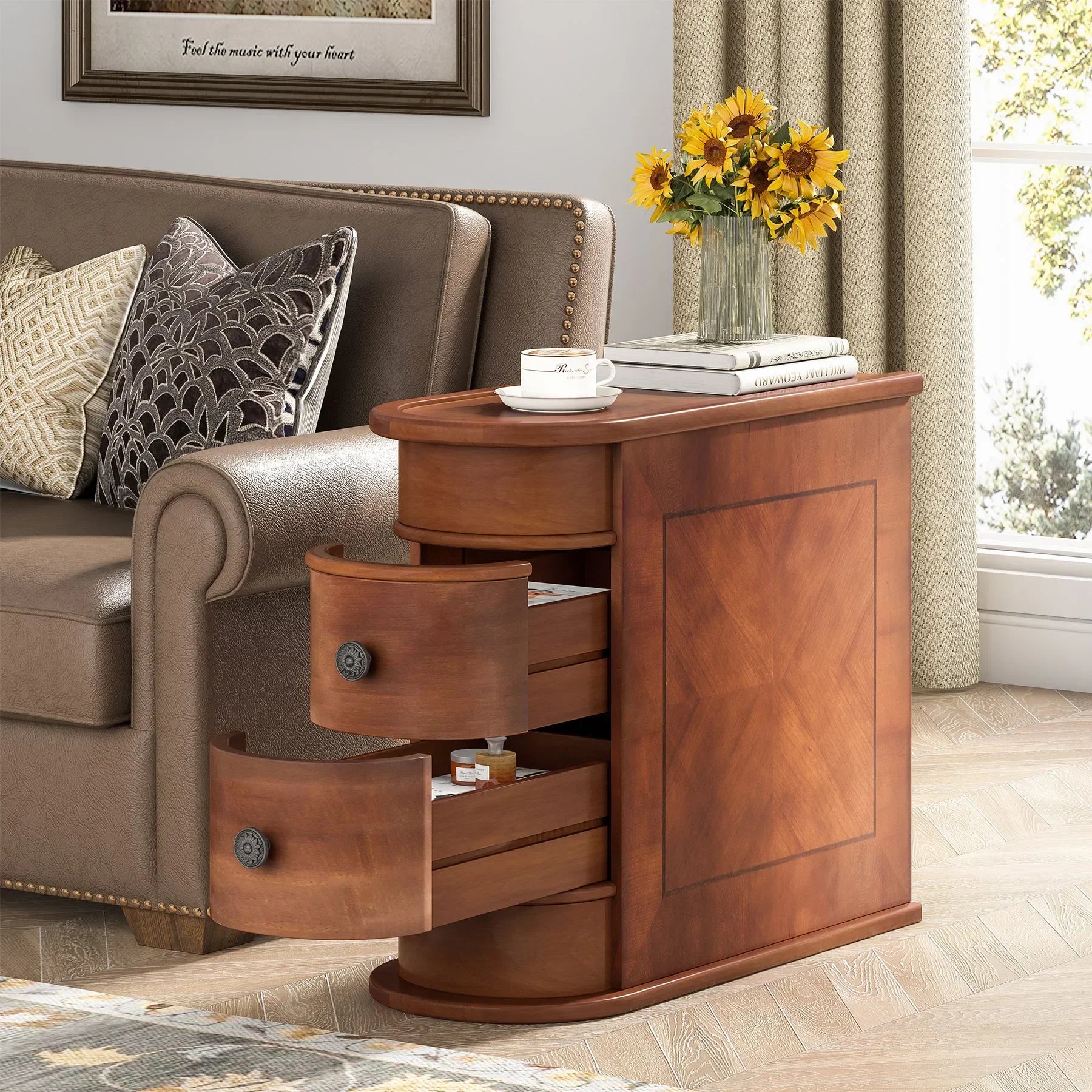 The Morsale Irvine Solid Wood Side Table with two open drawers stands beside a brown couch with patterned pillows. Complementing the minimalist decor, a vase with sunflowers, books, and a saucered cup soak in the sunlight warming this cozy living room.