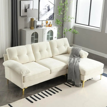 A modern living room showcases an 83" Morsale sectional sofa with a chaise in luxury chenille fabric adorned with a gray throw. Behind it, a white cabinet holds decorative items. Nearby are a tall lamp and potted plant, while a large window floods the space with natural light.
