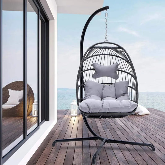 On a wooden deck overlooking the sea, Morsale's Patio Wicker Hanging Egg Chair with Stand offers relaxation. Crafted from PE Rattan and plush cushions, it's suspended from a sleek black metal stand. Large windows reflect the water view while a small lantern adds coziness to this serene haven.