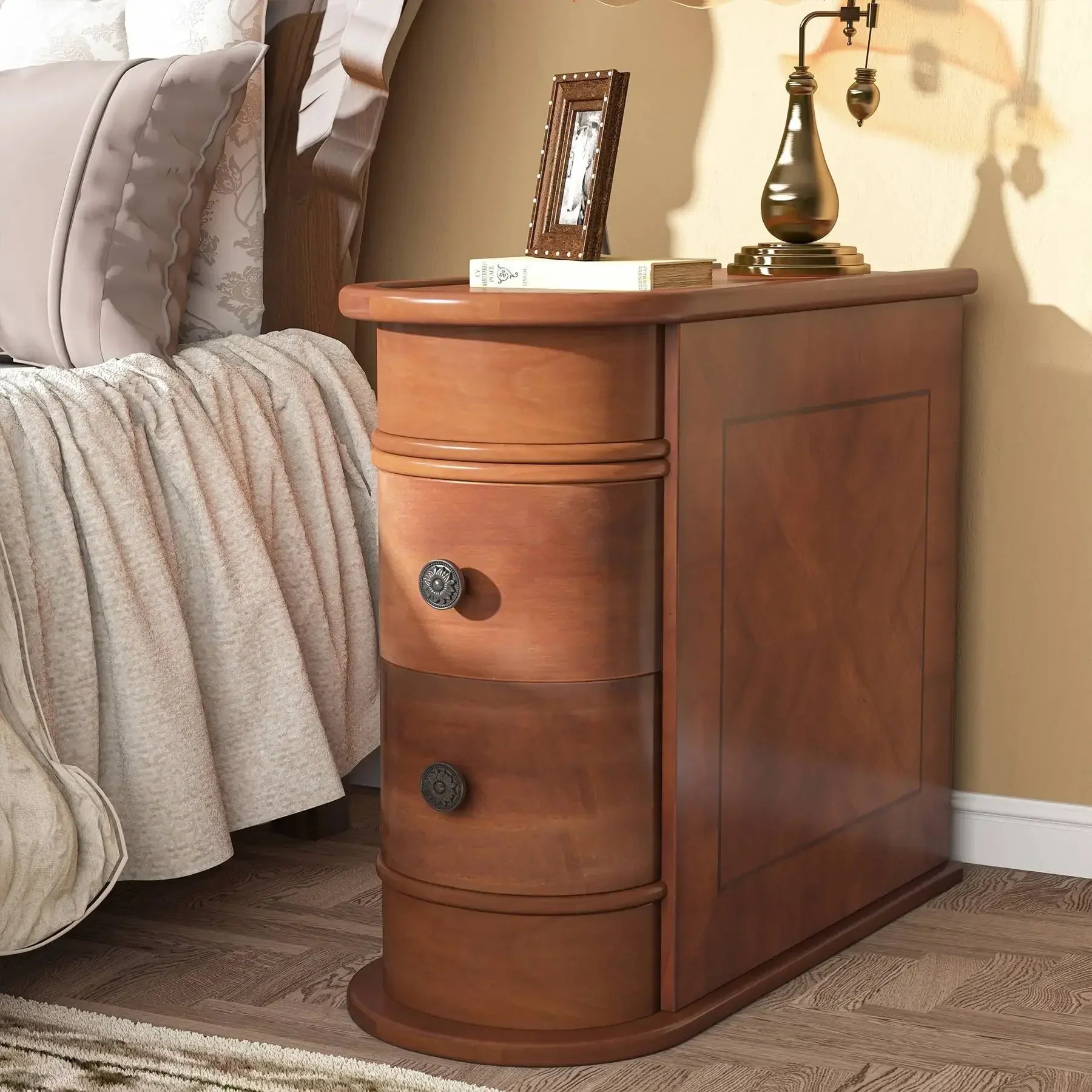 The Irvine Solid Wood Side Table by Morsale, featuring three drawers with round handles, holds a curved brass lamp and a small framed photo. Part of a bed with light-colored bedding is visible on the left.