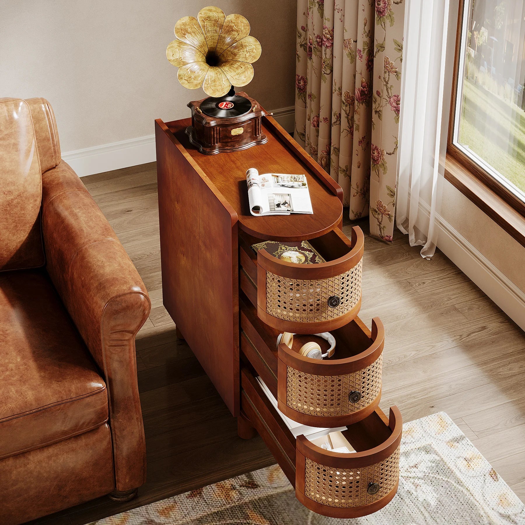 The Morsale Irvine Solid Wood Side Table with a vintage finish is beside a leather couch, topped with a gramophone and rolled papers. Inside the sliding drawers are a book and pocket watch. A curtain-draped window behind offers a charming garden view.