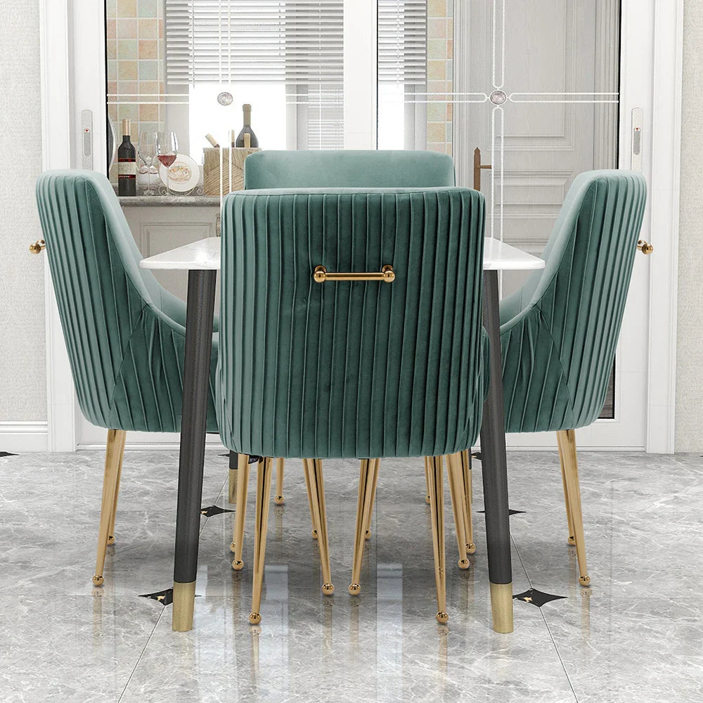 A dining room scene displays the Morsale Modern Glam Boucle Pleated Velvet Dining Chair Set of 4 in emerald green with gold legs around a sleek white table. The chairs offer vertical tufting, backrest handles, and sturdy construction. A window with wine bottles and marble floor tiles enhances the charm.
