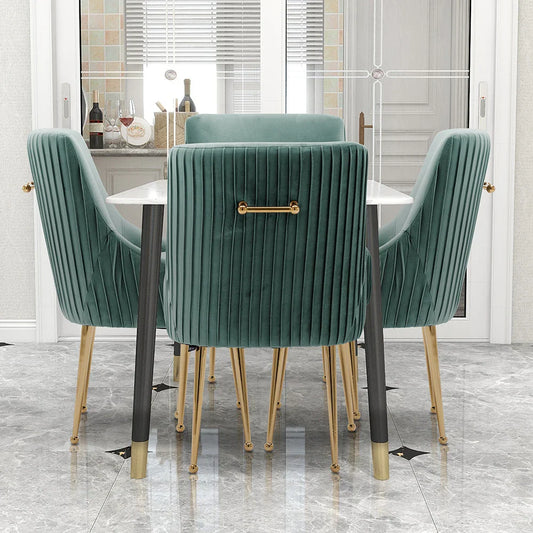 A dining room scene displays the Morsale Modern Glam Boucle Pleated Velvet Dining Chair Set of 4 in emerald green with gold legs around a sleek white table. The chairs offer vertical tufting, backrest handles, and sturdy construction. A window with wine bottles and marble floor tiles enhances the charm.