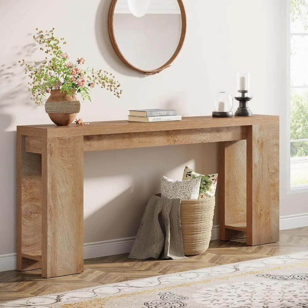 The Morsale Trenton 70-Inch Console Table, in modern style, leans against a white wall with a round mirror above. The tabletop features a potted plant and sleek candlesticks, while a woven basket below holds decorative pillows. A patterned floor completes the scene.
