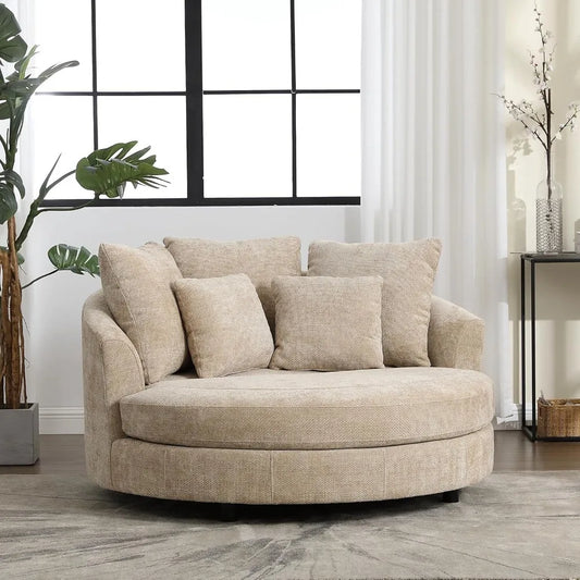 The 59.8" Oversized Accent Barrel Sofa Chair by Morsale, a cozy beige round swivel chair in modern style with cushions, sits invitingly in a bright living room. A large window with black framing and a potted plant adds charm, while a small table with decorative branches enhances the elegance on the hardwood floor.