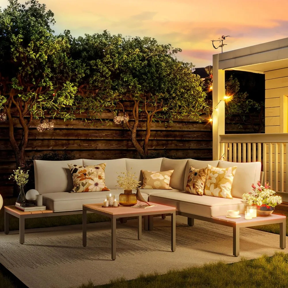 An outdoor patio featuring the Warton Patio Set by Morsale, with a beige all-weather sectional sofa, two patterned pillows, and a wooden coffee table holding snacks and drinks. Umbrellas and greenery create a serene garden ambiance.