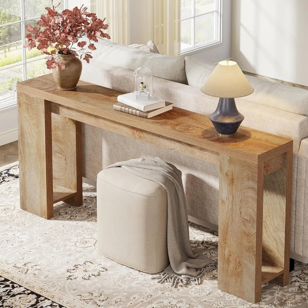 The Morsale Trenton 70-Inch Console Table, in modern style, leans against a white wall with a round mirror above. The tabletop features a potted plant and sleek candlesticks, while a woven basket below holds decorative pillows. A patterned floor completes the scene.
