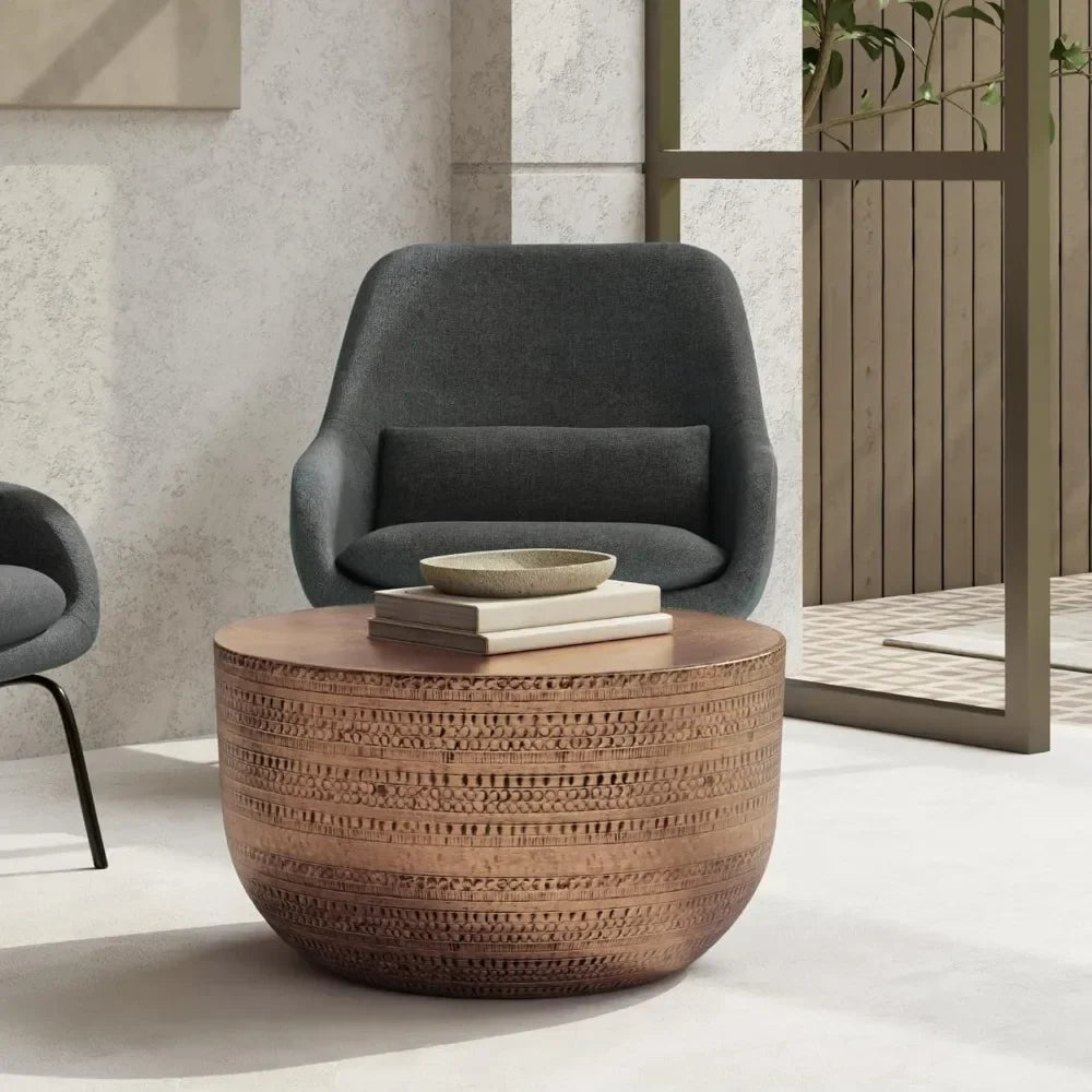 A cozy seating area features a Morsale Antique Copper Metal Coffee Table adorned with books and a ceramic bowl. By the glass door sits a gray upholstered armchair, leading to an outdoor space framed by wooden fencing, while copper accents add warmth to the scene.