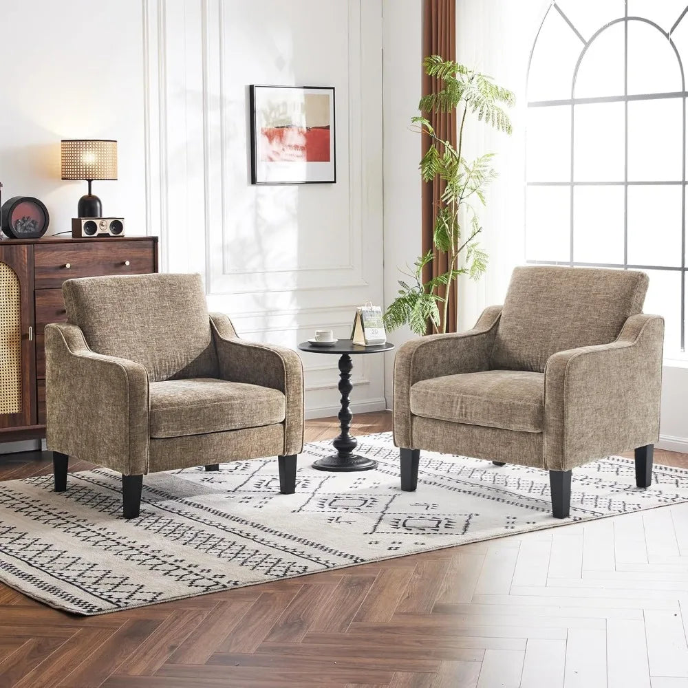 Two Morsale Living Room Armchairs, beige in color, rest on a patterned rug atop wooden flooring. A small black round table with a candle sits between them. The room includes a vintage cabinet, lamp, and large plant by the arched window—classic touches that don't require an assembly manual.