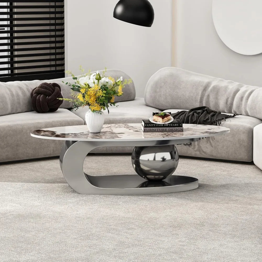 A modern living room showcases a light gray curved sectional sofa, reflecting Morsale's style commitment. An oval coffee table with a ceramic top and steel base sits on a gray rug, adorned with chemical-free yellow flowers. On the table rests "Vanity Theaters.