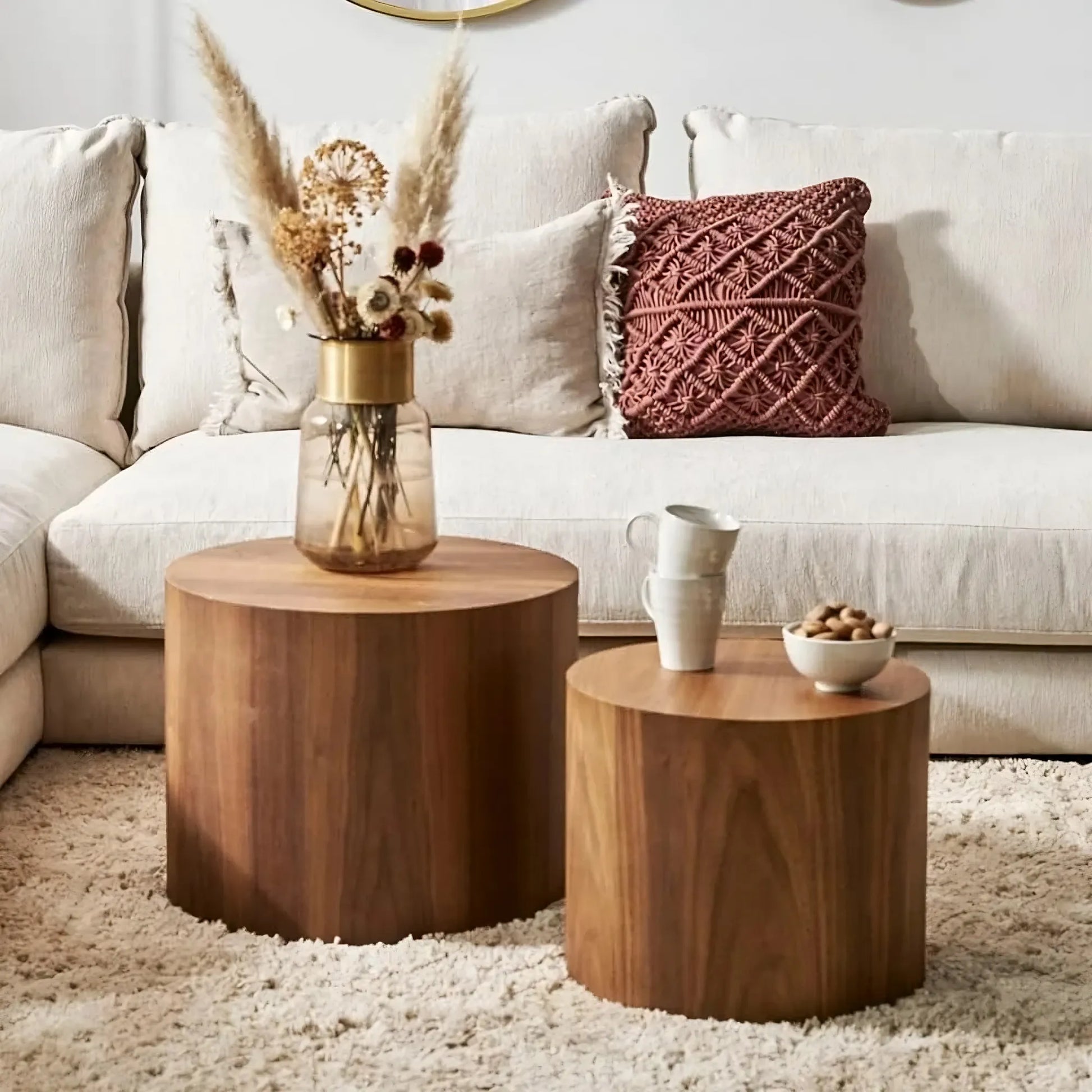 A cozy living room showcases a beige sectional sofa with Morsale's wood-accented Living Room Wood Coffee Tables, Set Of 2, adorned with dried flowers in a vase and small ceramic cups. A textured red cushion adds flair, while a soft beige rug completes the decor.
