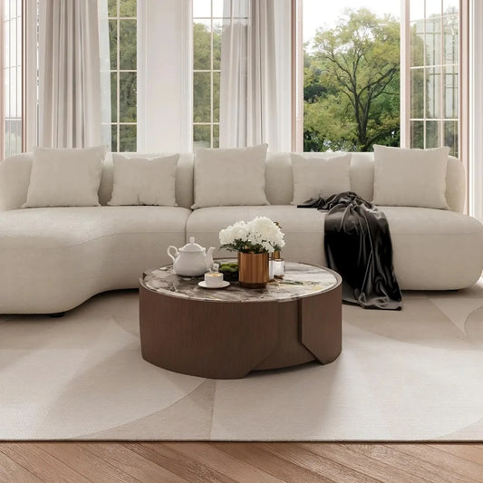 A modern living room showcases a curved white sofa with a dark throw on one end and a sleek 35" Modern Coffee Table by Morsale. The round table holds a teapot, cups, and a potted plant. Large windows reveal lush greenery outside.