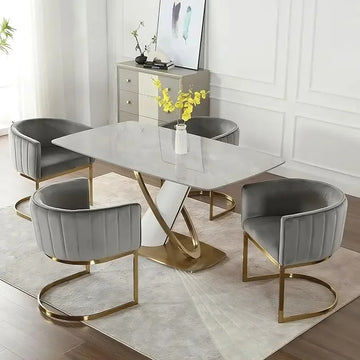 A modern dining room features a rectangular marble table with a gold twisted base, surrounded by four Morsale Modena Dining Chairs in gray linen. These chairs provide ergonomic support with cushioned seats and gold frames. A vase of yellow flowers sits on the table, complemented by abstract wall art.